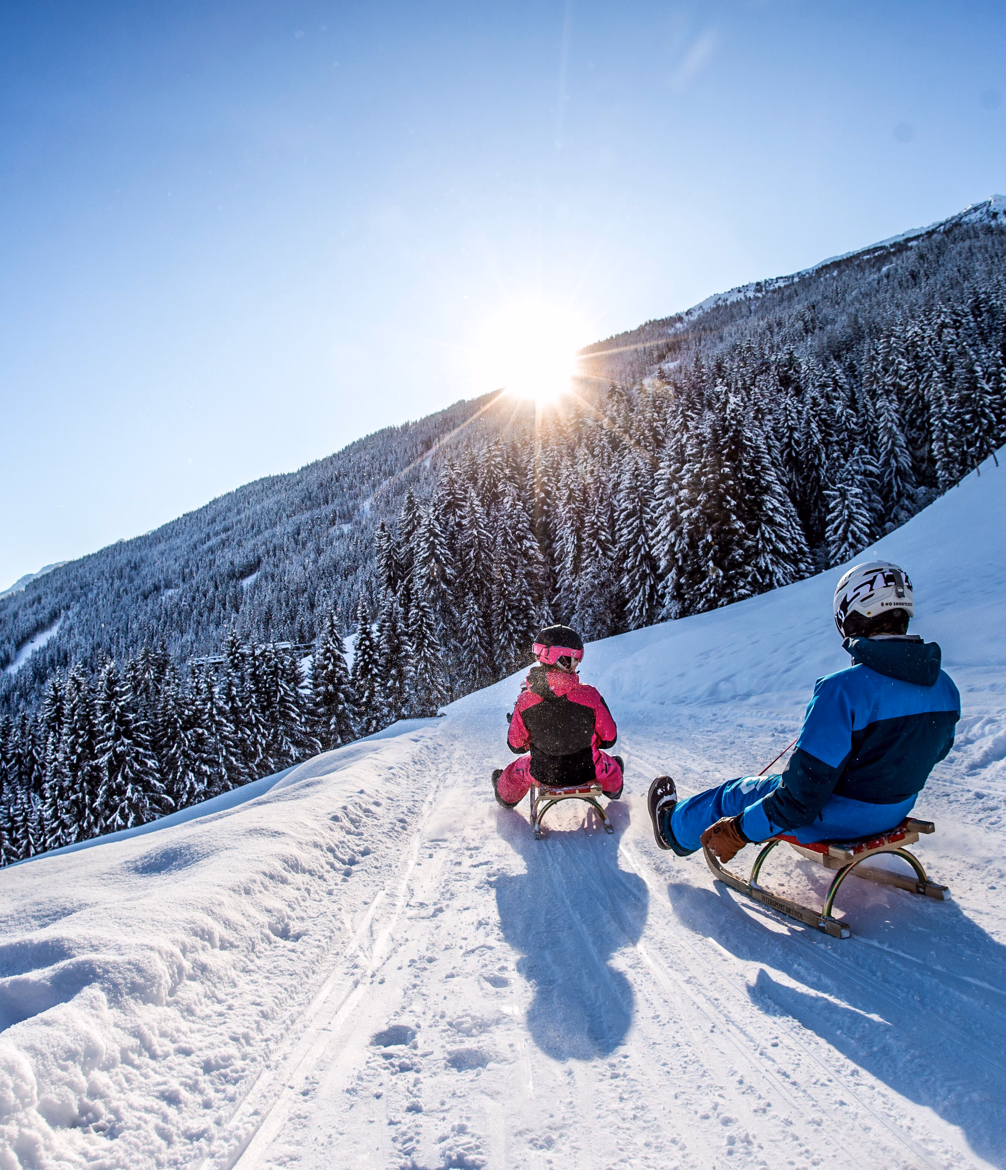 Zwei Rodler fahren auf verschneiter Rodelbahn am Spieljoch bei Sonnenschein durch die Winterlandschaft im Zillertal